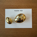 Two gold egg paperweights on a white card with 'THANK YOU' text, placed on a wooden surface.