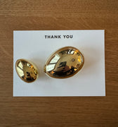 Two gold egg paperweights on a white card with 'THANK YOU' text, placed on a wooden surface.