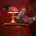 Person with tattooed hands interacting with a red lamp on a red surface.