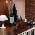 christmas decor midcentury inspo with wine bottle on a wooden surface with decorative items and a lamp.