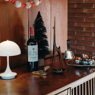 christmas decor midcentury inspo with wine bottle on a wooden surface with decorative items and a lamp.