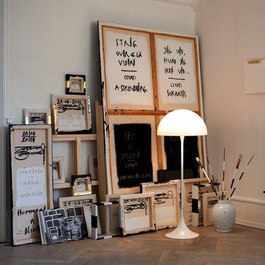 art studio interior with artworks, a  white panthella floor lamp, and decorative items on a wooden floor.