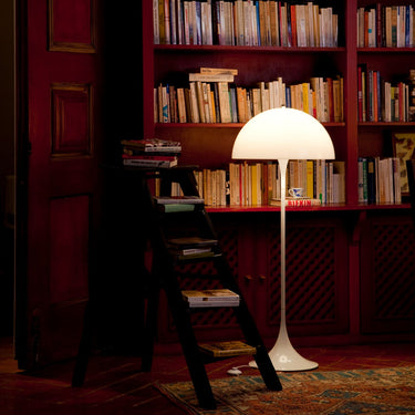 Home library filled with books in a dimly lit room with a 70s white floor lamp.