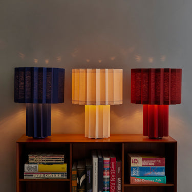 plissé pleated fabric table lamps lit up on a bookcase