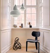 Modern interior with a black chair, decorative items, and pendant lights in a room with large windows.