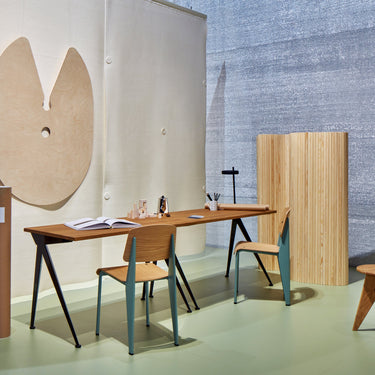 Modern office setup with long wooden desk, chairs, and stools against a textured wall.