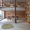 Modern interior with wooden bookshelves, a dining table, and large windows with rugs in neutral tones.