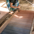 Person weaving on a traditional loom with blue and brown yarn.