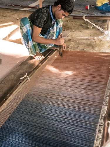 Person weaving on a traditional loom with blue and brown yarn.
