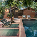 Outdoor setting with lounge chairs and rugs by a pool, surrounded by trees and buildings.