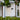 Front of a house with a white door and black sconce and window, surrounded by greenery.
