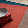 Stack of books and a bowl on a multicolored rug with a wooden floor.