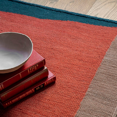 Stack of books and a bowl on a multicolored rug with a wooden floor.