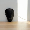 Black mask sculpture on a wooden surface with a light gray wall in the background