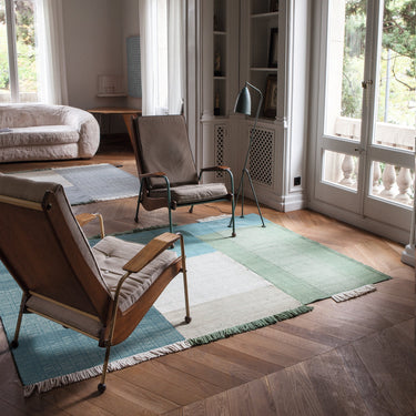 Living room with wooden floor, green rug, and jean prouvé chairs and royere sofa near large windows.