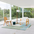 Modern living room with wooden chairs, a white sofa, and a lamp in a bright room with large windows.