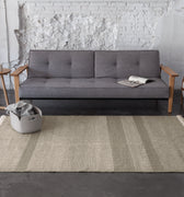 grey sofa with wood arms and a textured dhurrie rug on concrete floor