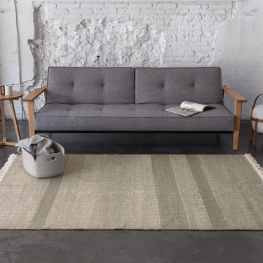 grey sofa with wood arms and a textured dhurrie rug on concrete floor
