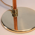 Close-up of a lamp with a gold base and copper-colored cord on a light background