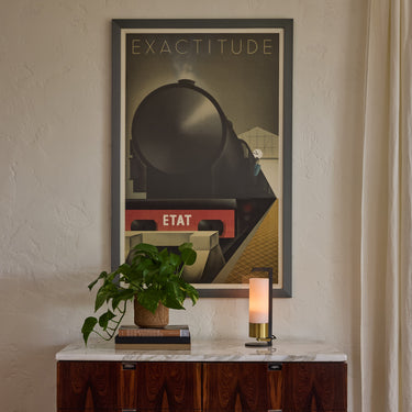 Wooden knoll credenza with marble top, plant, and lamp against a wall with a framed poster.