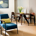 gueridon table in walnut with two standard chairs in a hotel room with a soft blue prouve armchair