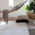 Hammock with pillows and a blanket in a room with light-colored walls and a plant. Wellness studio inspo.