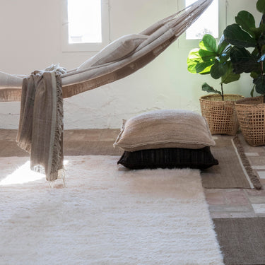 Hammock with pillows and a blanket in a room with light-colored walls and a plant. Wellness studio inspo.