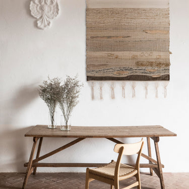 Wooden dining table with a chair in a room with a textured wall and decorative elements.