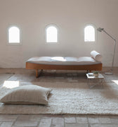 Minimalist bedroom with a bed, rug, and lamp in a bright room.