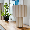 white textile plissé table lamp on a wooden surface with a blurred indoor background