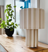 white textile plissé table lamp on a wooden surface with a blurred indoor background