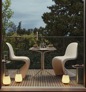 Modern outdoor patio with white chairs, table, and decorative elements near a large glass door.