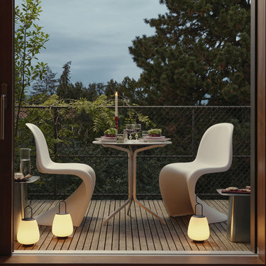 Modern outdoor patio with white chairs, table, and decorative elements near a large glass door.