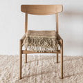 Wooden chair with a fringed blanket on a textured wool rug and light background