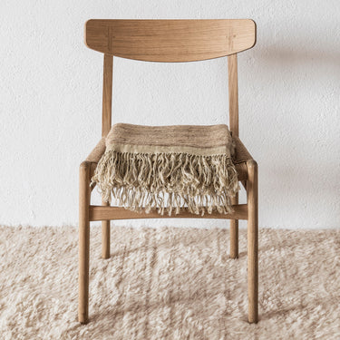 Wooden chair with a fringed blanket on a textured wool rug and light background